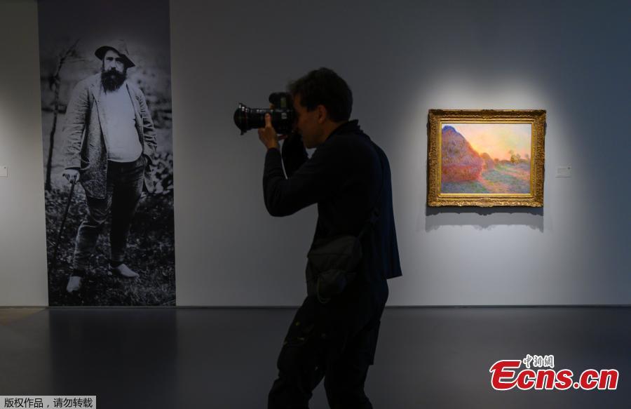 In this file photo taken on May 02, 2019, A photographer takes photos during a media preview, for Sotheby\'s Impressionist & Modern Art and Contemporary Art auctions, in New York. In the background is a picture of Claude Monet and one his famed Haystacks paintings. A Claude Monet painting from his \
