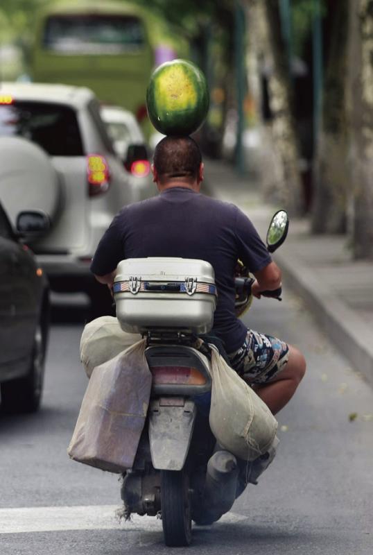 Hangzhou resident Wang Pinghua rides a motorcycle while balancing a watermelon on his head.   (Photo provided to China Daily)