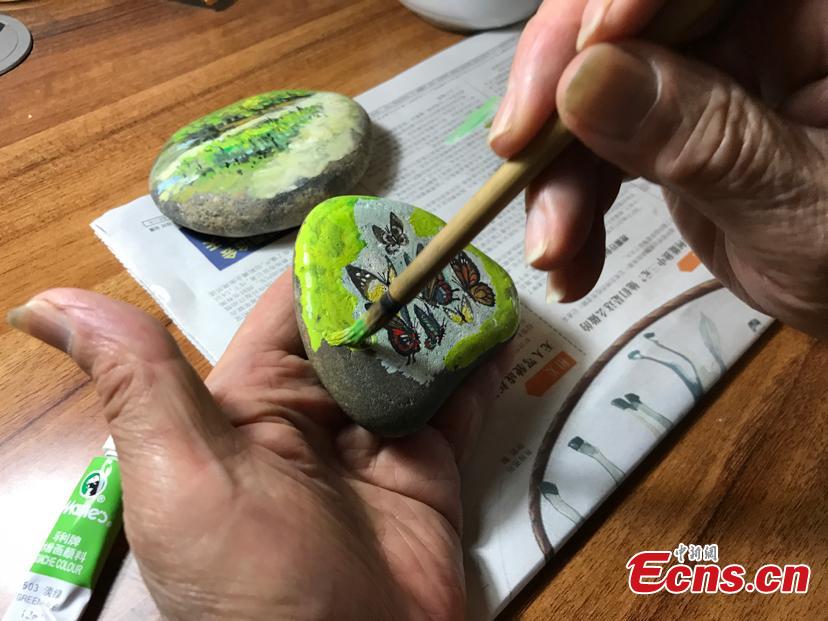 Zhang Yulin gives a final touch on his painting on a stone. Zhang Yulin, 81, from southwest China’s Chongqing municipality, collects stones from the Yangtze River banks and turns them into artworks with paintings.  (Photo: China News Service/ Xiao Jiangchuan)