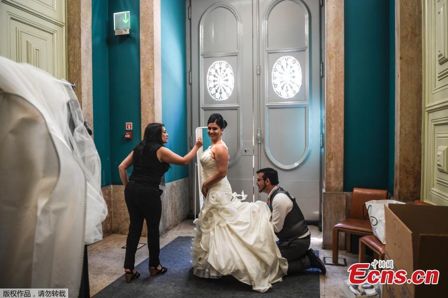 A bridal gown designer helps a bride to get dressed before celebrating a multiple civil ceremony at the Lisbon\'s city hall, during Saint Anthony\'s day on June 12, 2019. It is Lisbon\'s wedding of the year. Crowds gather at the cathedral, hoping to catch a glimpse of the newlyweds as cameras lie in wait. Then not one, but 11 couples walk out, fresh from tying the knot today in an all-expenses-paid ceremony, the beneficiaries of a decades-long annual tradition that fetes the Portuguese capital\'s beloved patron Saint Anthony, matchmaker extraordinaire. (Photo/Agencies)