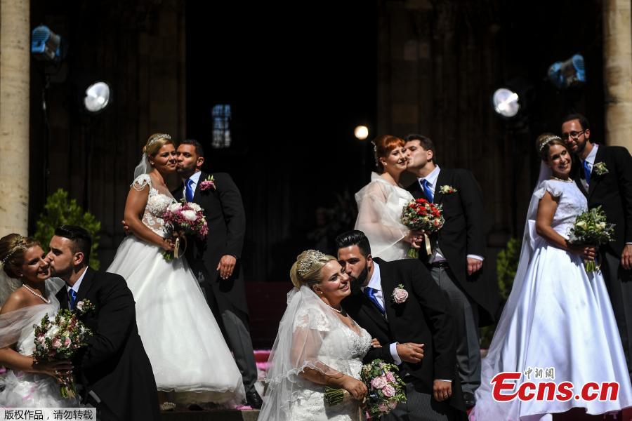 Brides and grooms kiss as they pose for a photo outside the Lisbon\'s Cathedral following their wedding ceremony in Lisbon on June 12, 2019. It is Lisbon\'s wedding of the year. Crowds gather at the cathedral, hoping to catch a glimpse of the newlyweds as cameras lie in wait. Then not one, but 11 couples walk out, fresh from tying the knot today in an all-expenses-paid ceremony, the beneficiaries of a decades-long annual tradition that fetes the Portuguese capital\'s beloved patron Saint Anthony, matchmaker extraordinaire.(Photo/Agencies)
